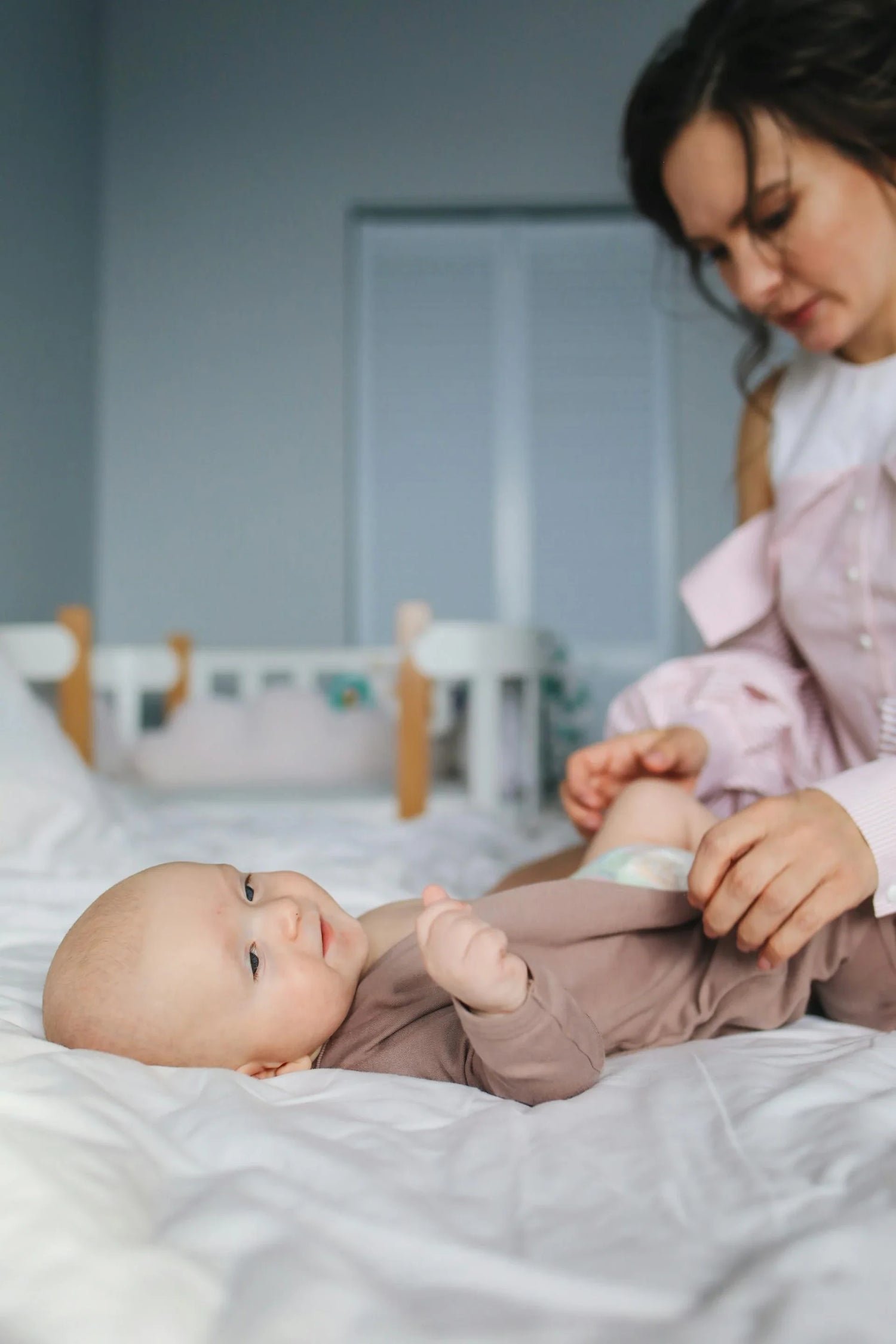 Mom changing baby's diaper on a cozy bed, featuring soft organic baby clothing, essential diapering supplies for newborns and infants, comfortable and practical baby care.