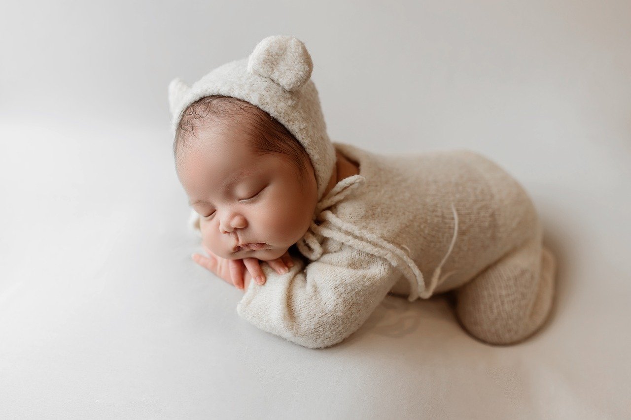 Newborn baby sleeping in a cozy bear-ear onesie, soft and breathable baby sleepwear, organic cotton outfit for newborns, perfect for photoshoots and comfort.