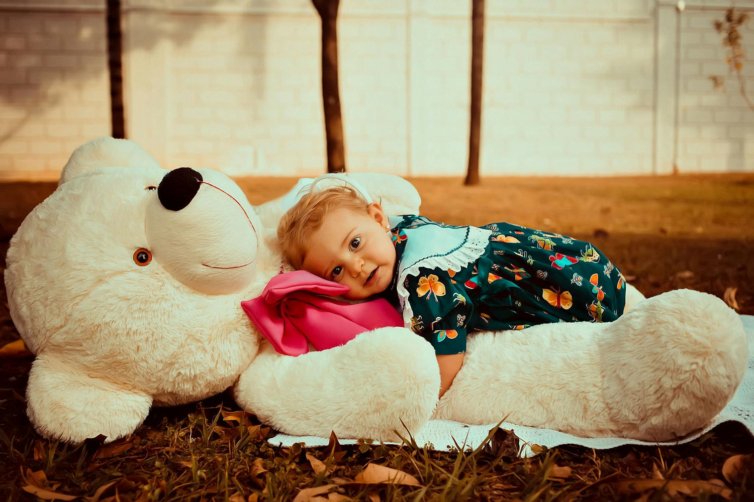 Toddler wearing a floral romper while resting on a giant teddy bear, featuring stylish and comfortable rompers for babies and toddlers, perfect for playtime and outdoor activities.