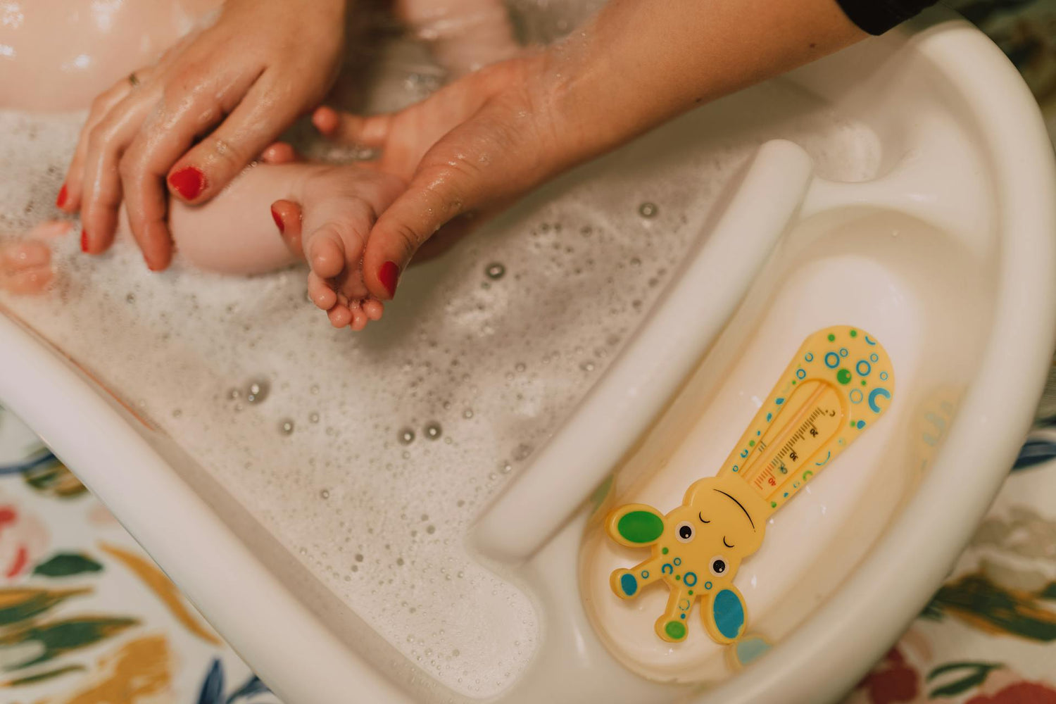 Baby bath time with hands gently washing in a baby bathtub, featuring a cute animal-themed bath thermometer, safe and comfortable bathing essentials for infants.