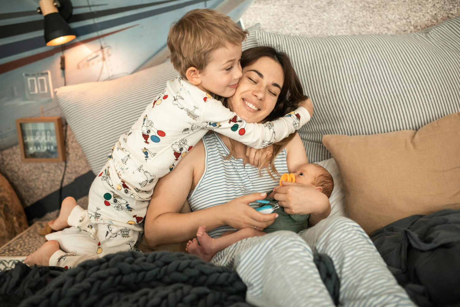 Mom cuddling with toddler in printed pajamas and newborn baby in soft onesie, featuring cozy and stylish baby and children's clothing perfect for bedtime comfort.